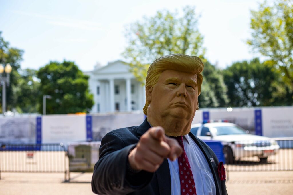 Person wearing a Donald Trump mask and pointing in front of the White House